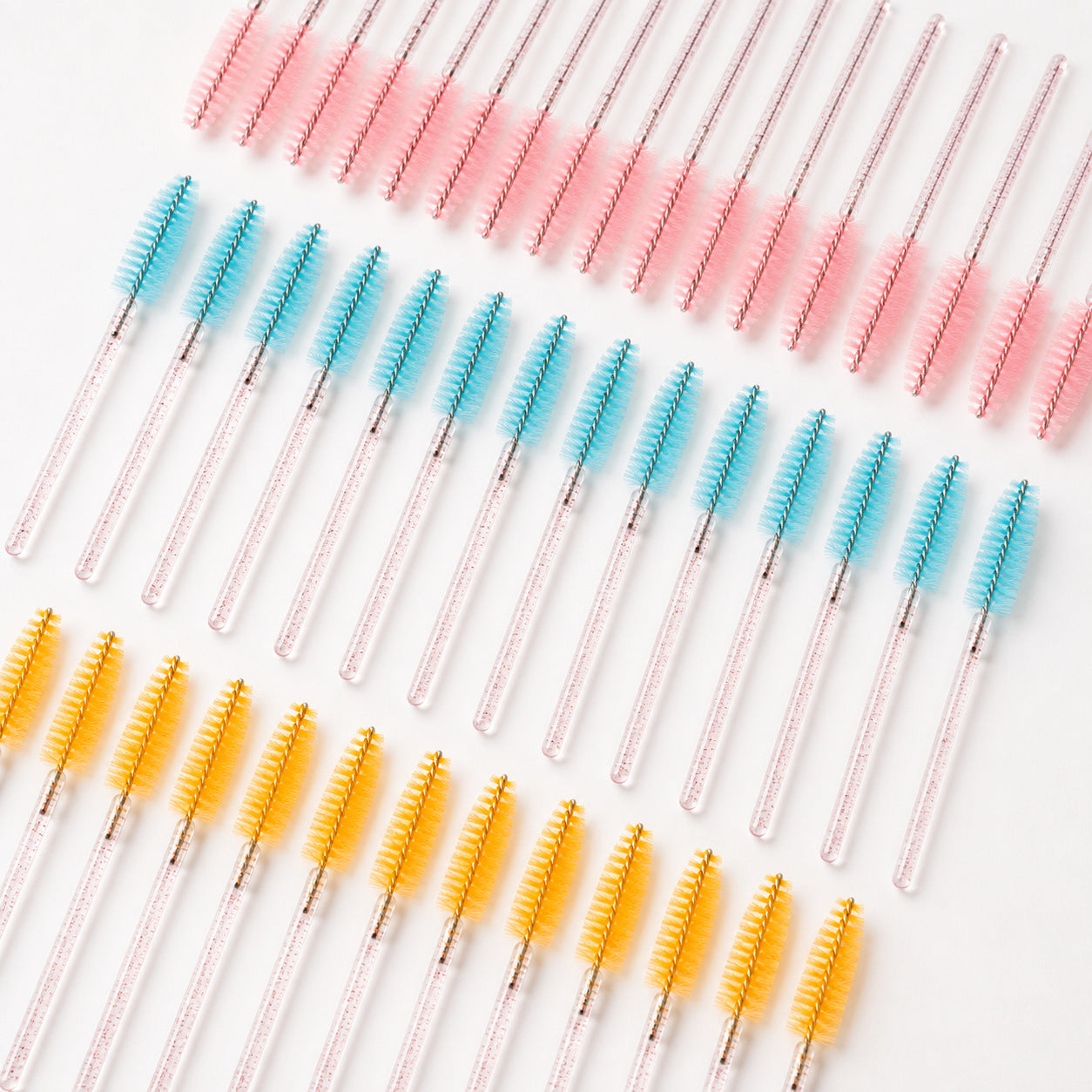 Disposable eyelash spoolie brushes arranged by pink, blue and yellow color